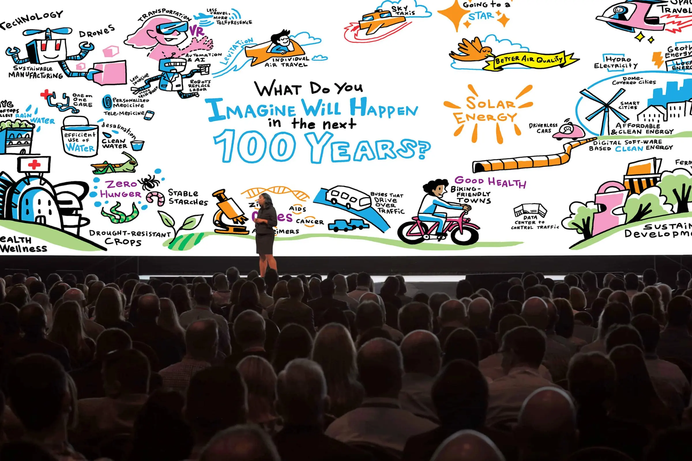 A packed conference hall watches a speaker on stage beneath a giant ImageThink drawing projected across the screen.