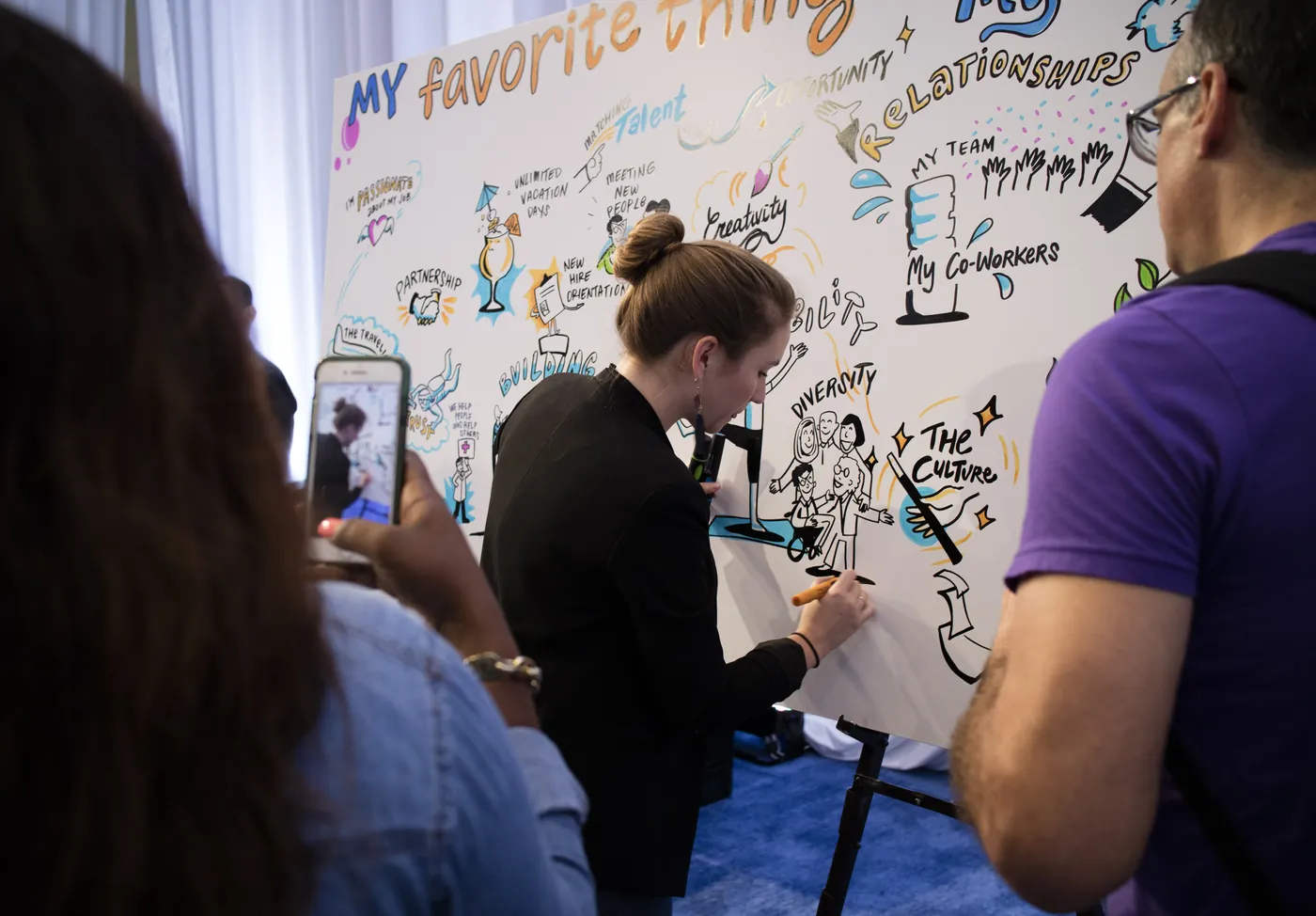 Attendees watch and photograph an ImageThink artist drawing a live mural.