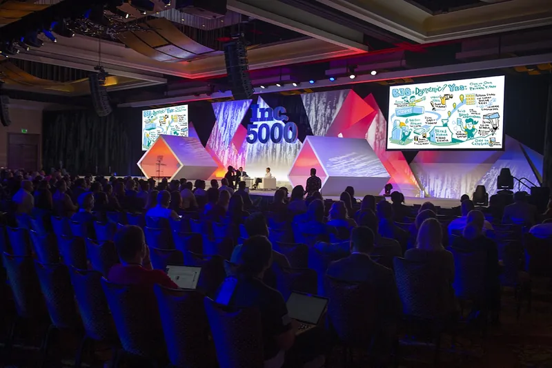 A packed Inc. 5000 conference hall with ImageThink drawings on the big screens beside the stage.