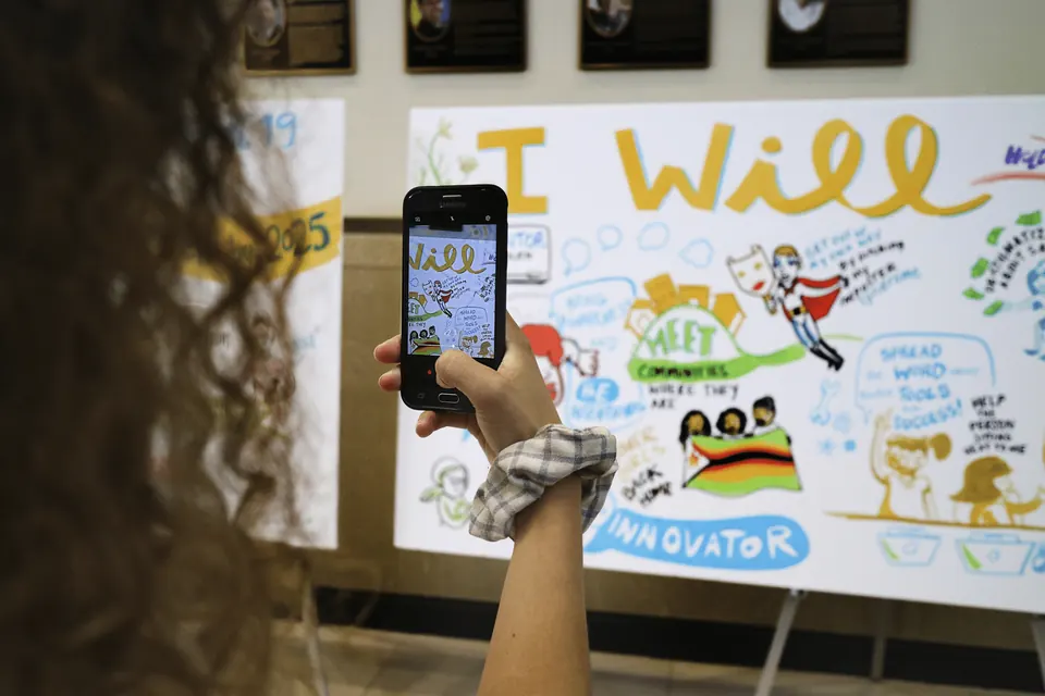 A nonprofit attendee photographing a colorful commitment mural